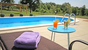 A poolside area with a lounge chair, a purple towel, and two drinks on a small table. - Apartment in Sveti Petar u Sumi (Sveti Petar u Sumi)
