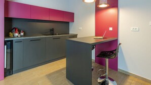 A modern kitchen with grey cabinets, a black countertop, and a red accent wall. There is a laptop on the countertop and a bar stool with a black seat. - Apartment in Sveti Petar u Sumi (Sveti Petar u Sumi)