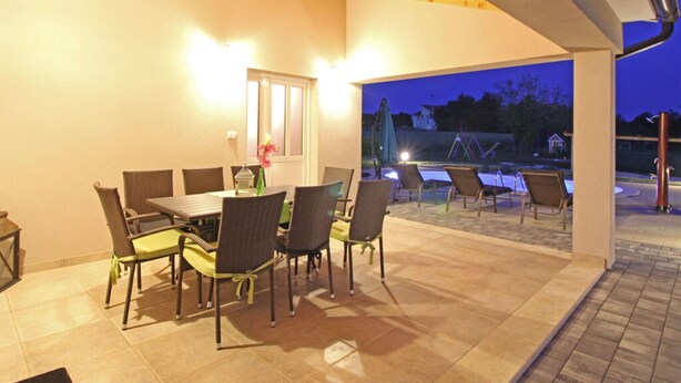 An outdoor patio with a dining table and chairs, a small table with a vase, and a view of a playground in the background. - Apartment in Sveti Petar u Sumi (Sveti Petar u Sumi)
