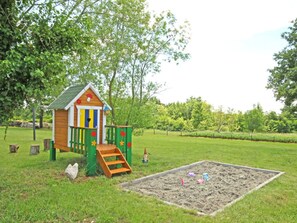Children can play in the playhouse and sandbox surrounded by a lush garden and trees.