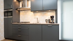A modern kitchen with dark cabinets, a stainless steel range hood, and a coffee maker on the counter. - Holiday Home in De Cocksdorp (De Cocksdorp)
