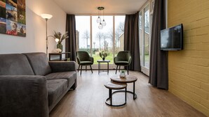 A modern living room with a sofa, two chairs, a coffee table, and a TV mounted on the wall. - Holiday Home in De Cocksdorp (De Cocksdorp)