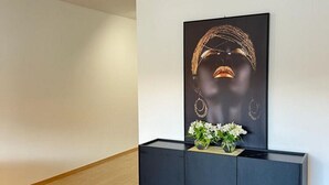 Une pièce moderne avec une console noire, une œuvre d’art encadrée et un vase contenant des fleurs blanches.
