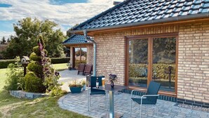 A house with a brick exterior, large glass sliding doors, and a patio area with outdoor furniture. - Rugen Apartment Waterview (Bergen auf Ruegen)