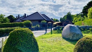 A house with a tiled roof, surrounded by well-maintained hedges and a large rock. - Rugen Apartment Waterview (Bergen auf Ruegen)