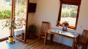 A room with a wooden floor, a table with chairs, a window with a view of greenery, and a potted plant. - Rugen Apartment Waterview (Bergen auf Ruegen)