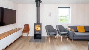 Un salon moderne avec un poêle à bois, un téléviseur à écran plat, un canapé et deux fauteuils.