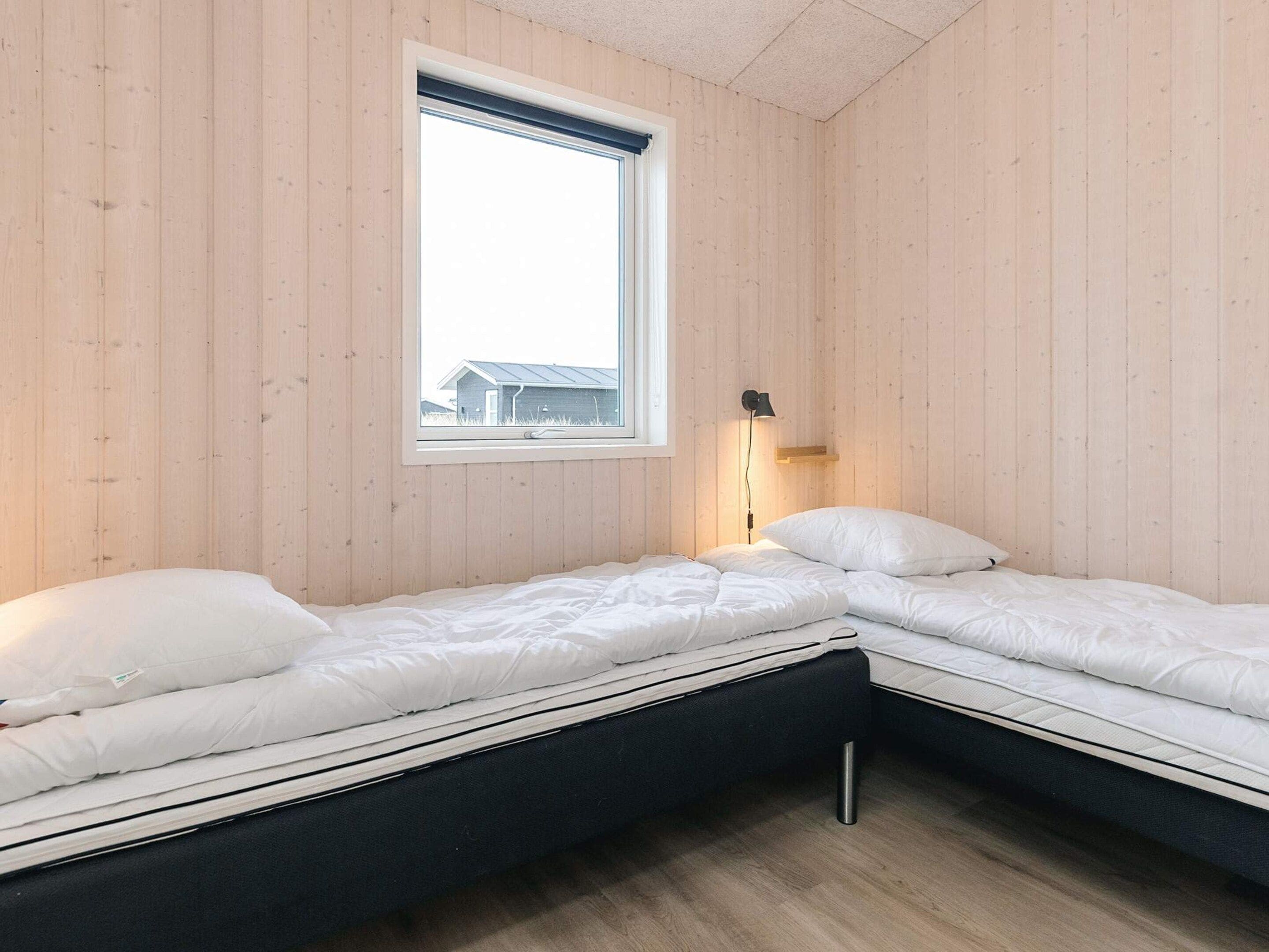 Pieni, yhden huoneen asunto, jossa on kaksi sänkyä, ikkuna ja seinään kiinnitetty valaisin.