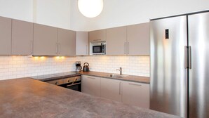 Une cuisine moderne dotée d’un îlot central, d’appareils électroménagers en acier inoxydable et d’un luminaire suspendu.