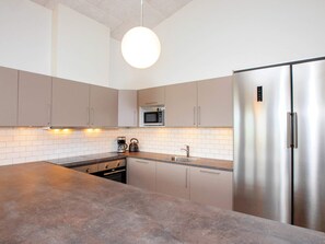 A modern kitchen with a central island, stainless steel appliances, and a hanging light fixture. - 5 Star Holiday Home in Lokken (Lokken)