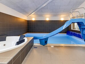 An indoor swimming pool with a blue slide, a hot tub, and tiled walls. - 5 Star Holiday Home in Lokken (Lokken)