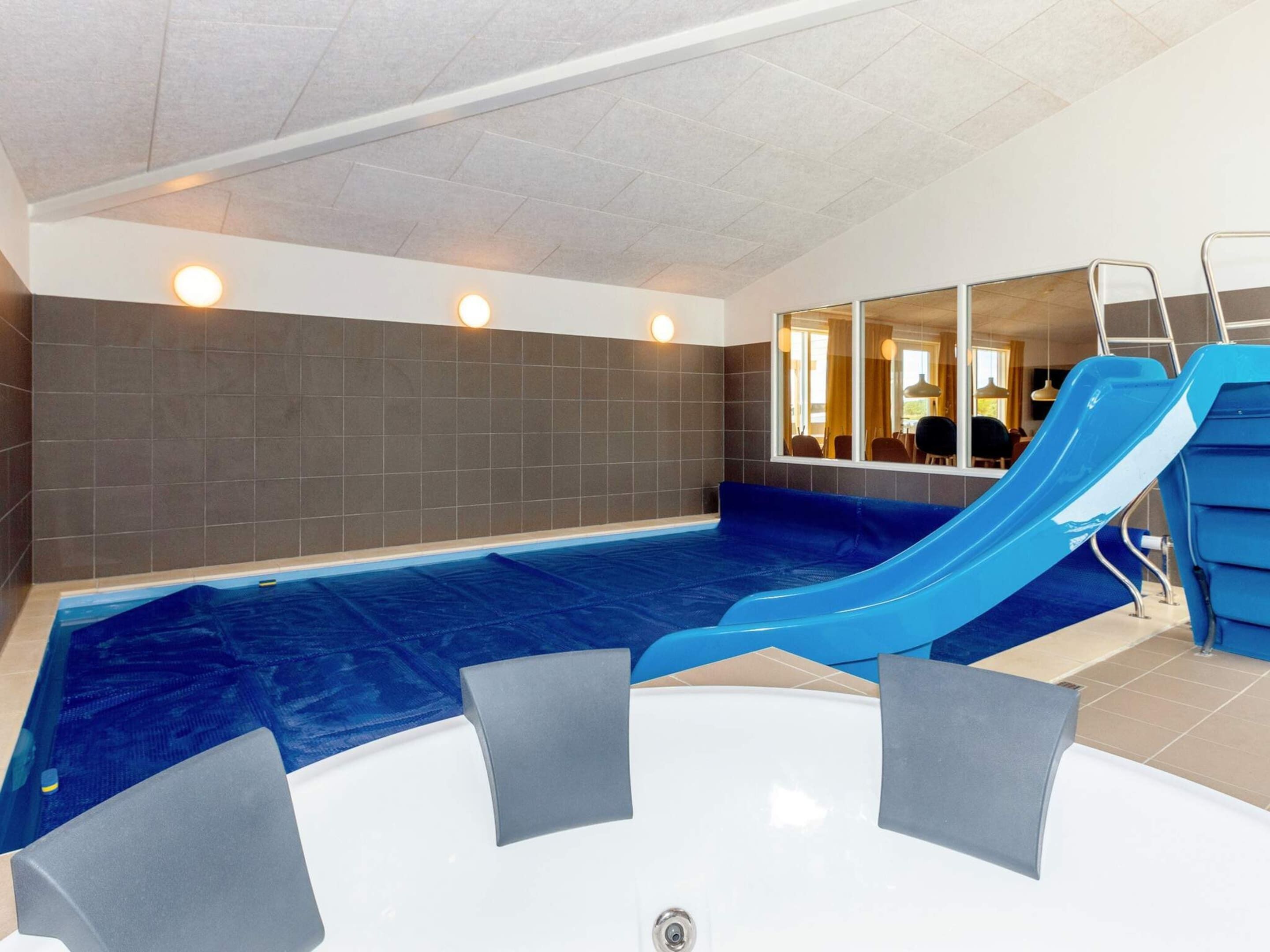 Une piscine intérieure avec un toboggan bleu, un jacuzzi et une vue sur l’intérieur.