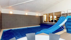 Une piscine intérieure avec un toboggan bleu, un jacuzzi et une vue sur l’intérieur.