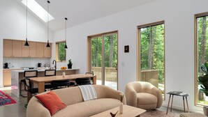 A modern living room with a sofa, coffee table, and a dining area with a table and chairs. - Architect-Designed 3BR Forest Retreat Near Asheville (Weaverville)