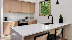 A modern kitchen with wooden cabinets, a white marble countertop, a sink, and two pendant lights. - Architect-Designed 3BR Forest Retreat Near Asheville (Weaverville)