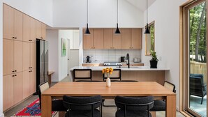 A modern kitchen with wooden cabinets, a central island, and pendant lighting. - Architect-Designed 3BR Forest Retreat Near Asheville (Weaverville)