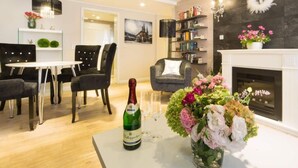 A modern living room with a fireplace, a dining area with a table and chairs, and a bookshelf filled with books. - Sky Lodge Holiday Apartment (Wernigerode)