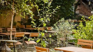 An outdoor seating area with wooden tables and chairs, surrounded by potted plants and a rustic brick wall. - Sky Lodge Holiday Apartment (Wernigerode)