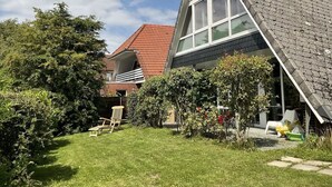 Et moderne hus med skråtag, et stort vindue og en velholdt have med græsplæne og en træstol.