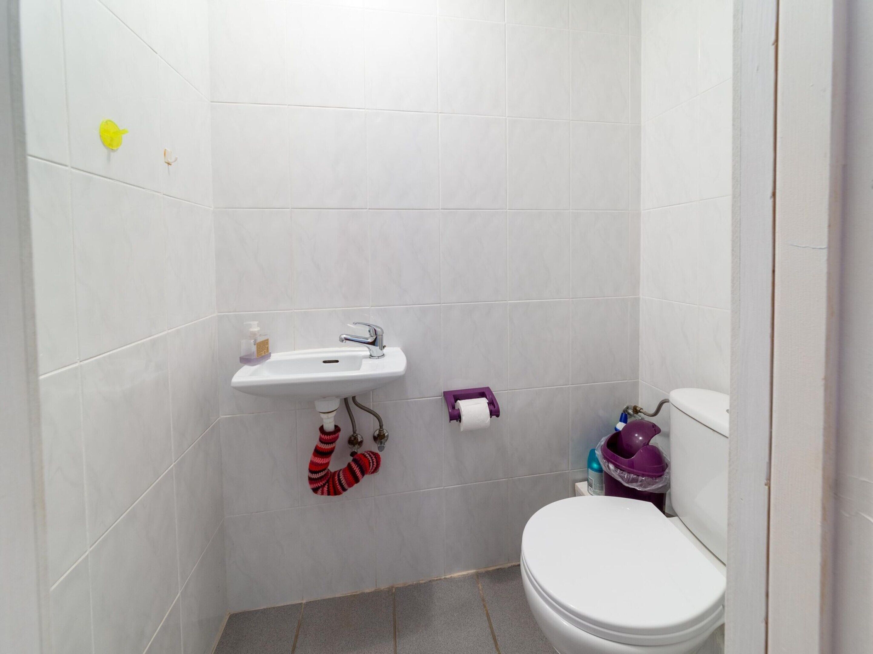 A small bathroom with a white sink, toilet, and a purple cleaning bucket.