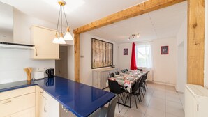Una cocina moderna con encimera azul, vigas de madera y zona de comedor con mesa para seis.