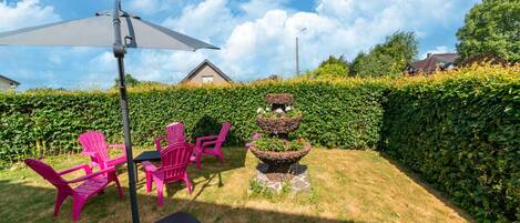 A garden with a patio area featuring a table, chairs, and an umbrella.