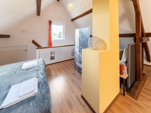 A room with a bed, a window with curtains, a radiator, and a wooden ceiling.