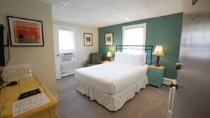 A hotel room with a bed, two bedside tables with lamps, a chair, a desk with a remote control, and a stack of towels.