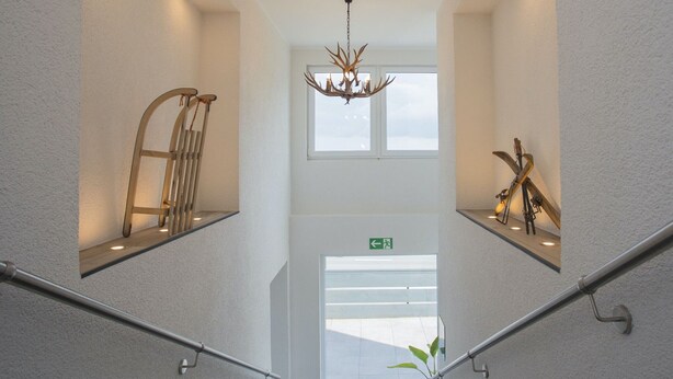 Un intérieur moderne avec un escalier central, des rampes en métal et un lustre.