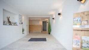 Un couloir avec un plancher en bois, un paillasson noir, une plante en pot et une armoire en bois remplie de livres.