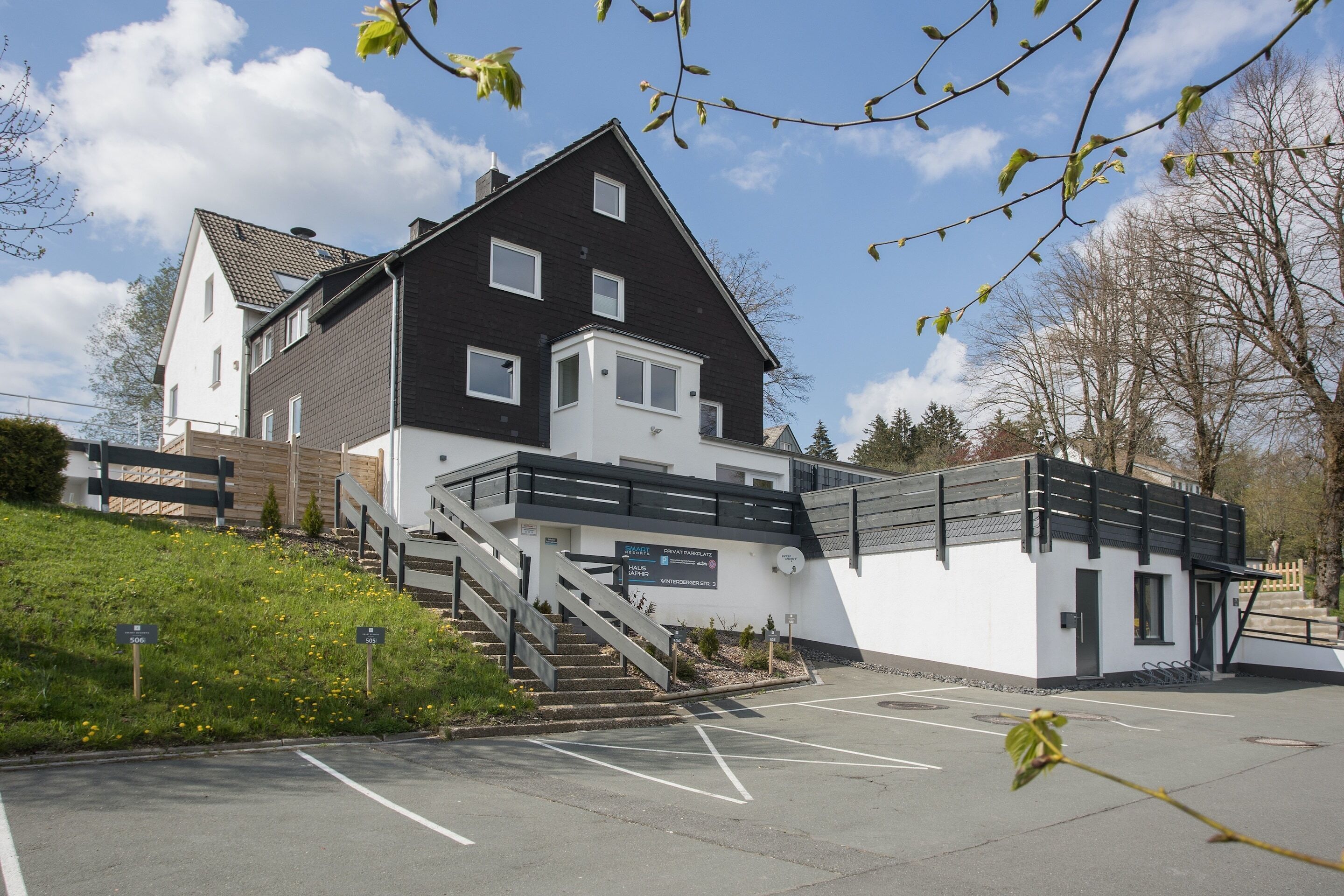 Un bâtiment à deux étages, avec un escalier menant à l’entrée, un parking et une enseigne indiquant le nom du bâtiment.