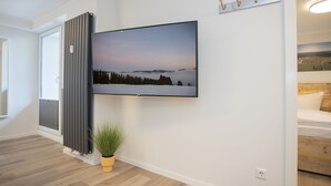 Un salon moderne avec un grand téléviseur à écran plat fixé au mur, une plante en pot et un plancher en bois.