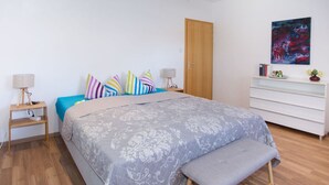 Een slaapkamer met een bed, een bankje, een kaptafel en een schilderij aan de muur.