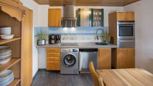 Een kleine keuken met houten kastjes, een RVS vaatwasser, een wasmachine en een inbouwoven.