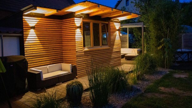 Een modern houten huis met een patio, inclusief een bank en een tafel.