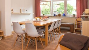 Een moderne eetruimte met een houten tafel en stoelen, een bankje, en uitzicht op het landschap door grote ramen.