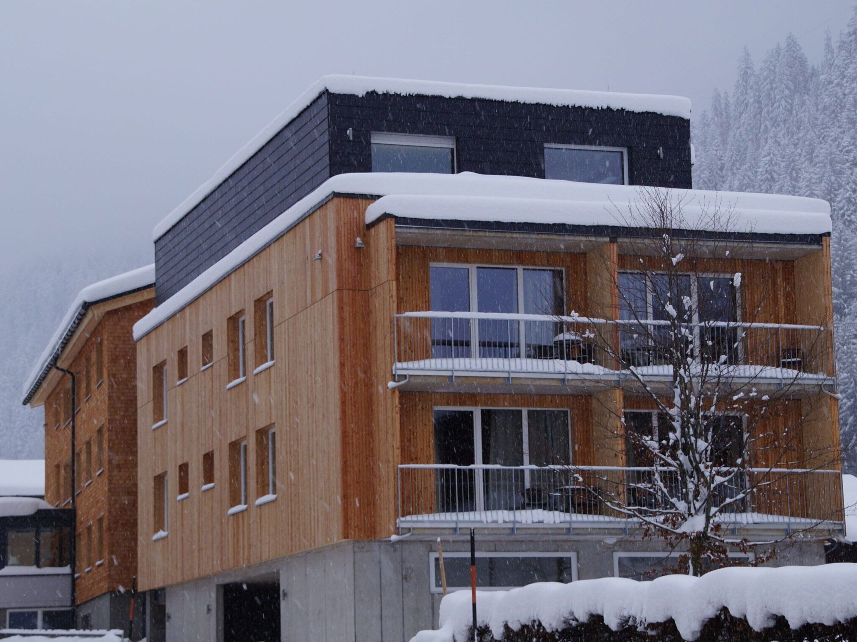A modern multi-story building with a wooden facade and balconies, surrounded by snow.