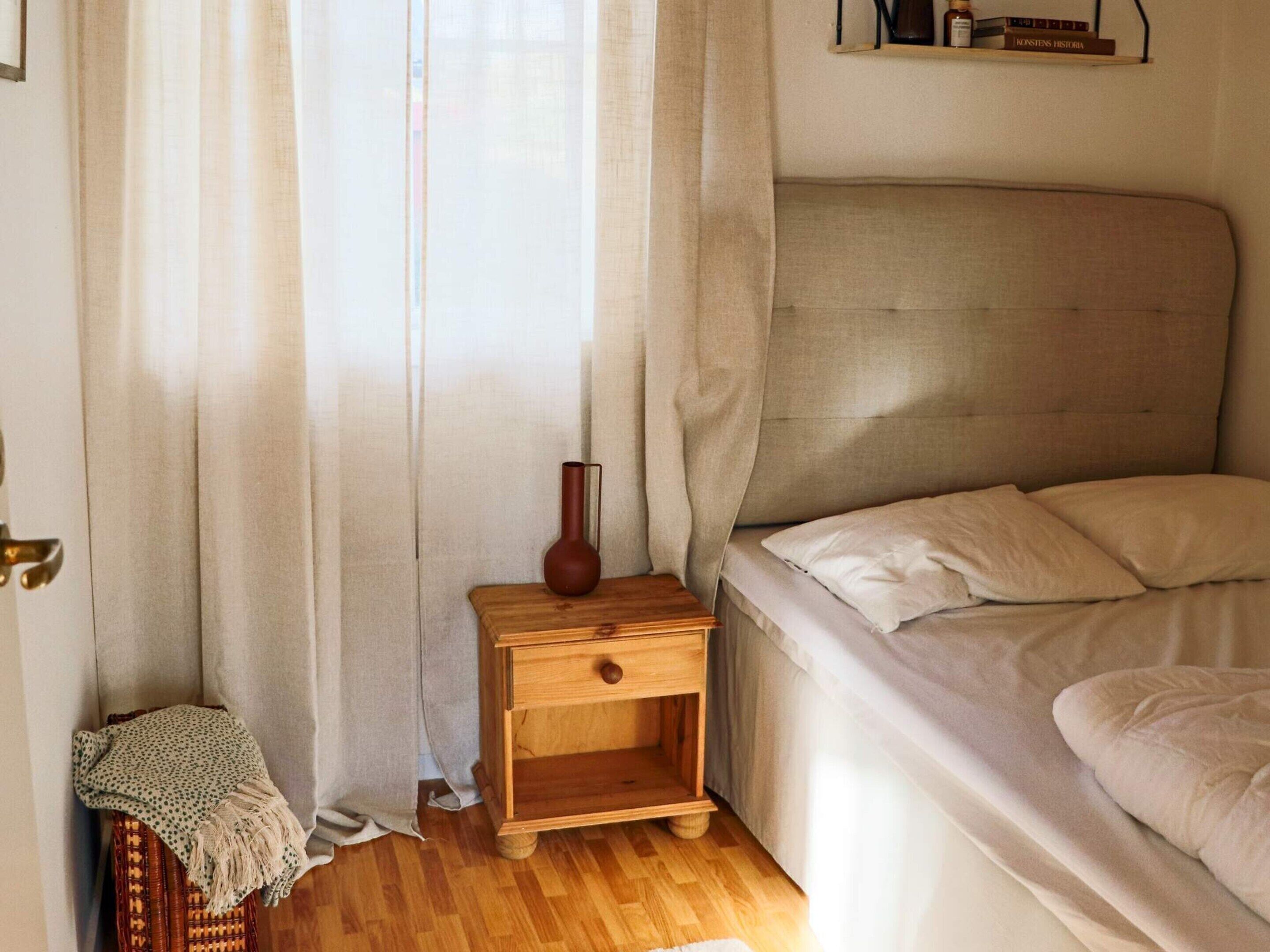 Una camera da letto con un letto, un comodino, un vaso e una poltrona in vimini.