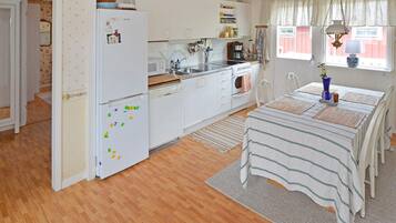 A kitchen with white cabinets, a refrigerator with magnets, a microwave, and a sink. There's a dining table with a striped tablecloth and chairs.