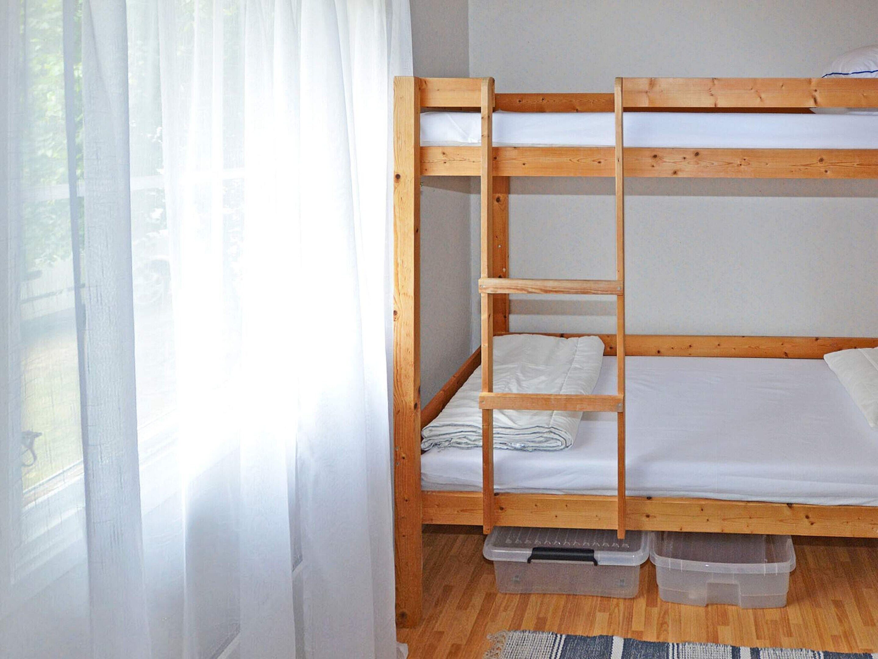 Un lit superposé avec une échelle, du linge de lit blanc et des bacs de rangement sous le lit du bas.