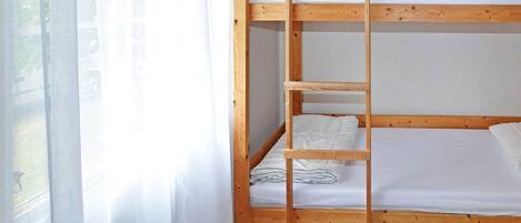 Un lit superposé avec une échelle, du linge de lit blanc et des bacs de rangement sous le lit du bas.