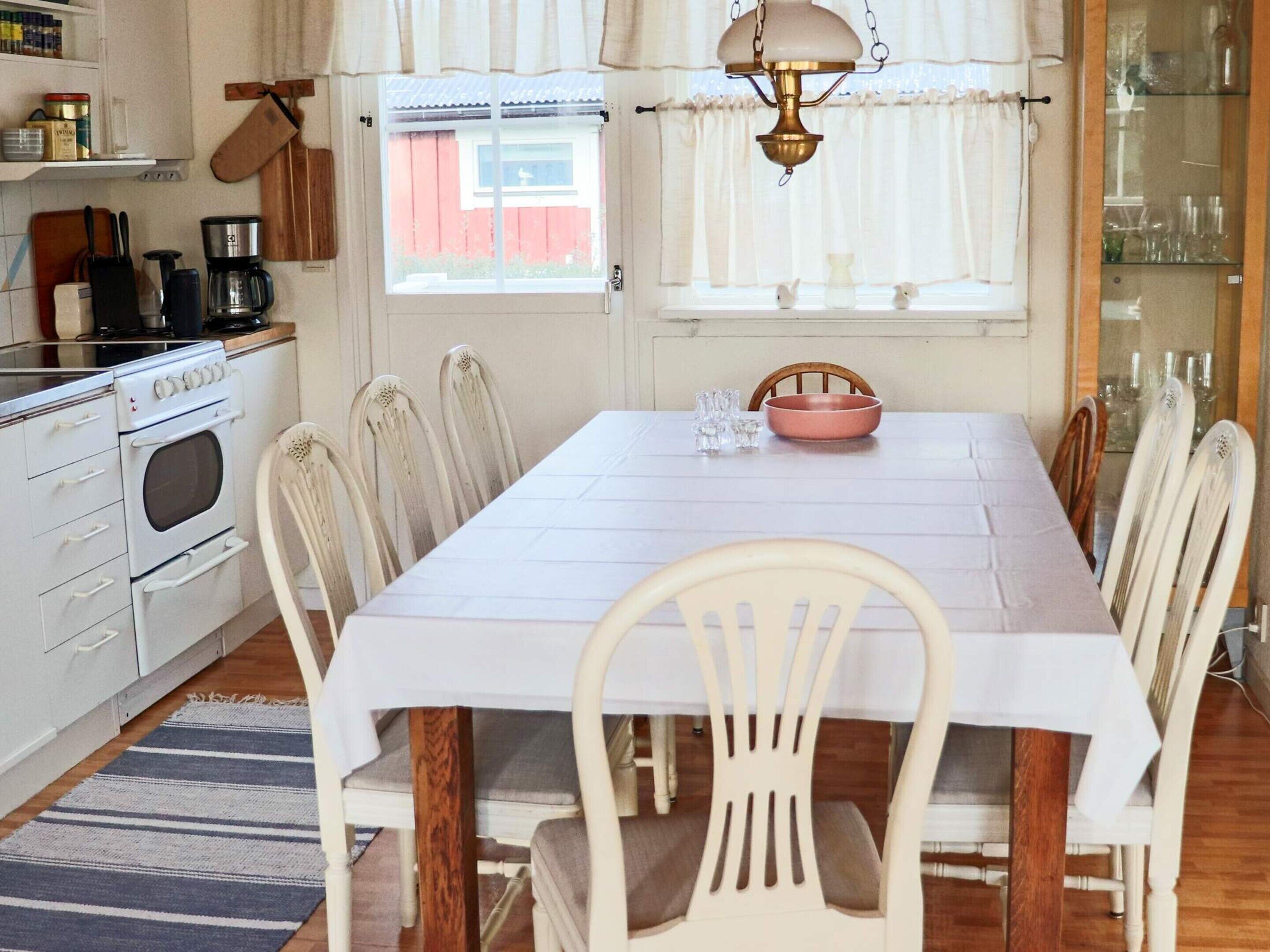 A dining area with a white table, chairs, and a kitchen in the background.