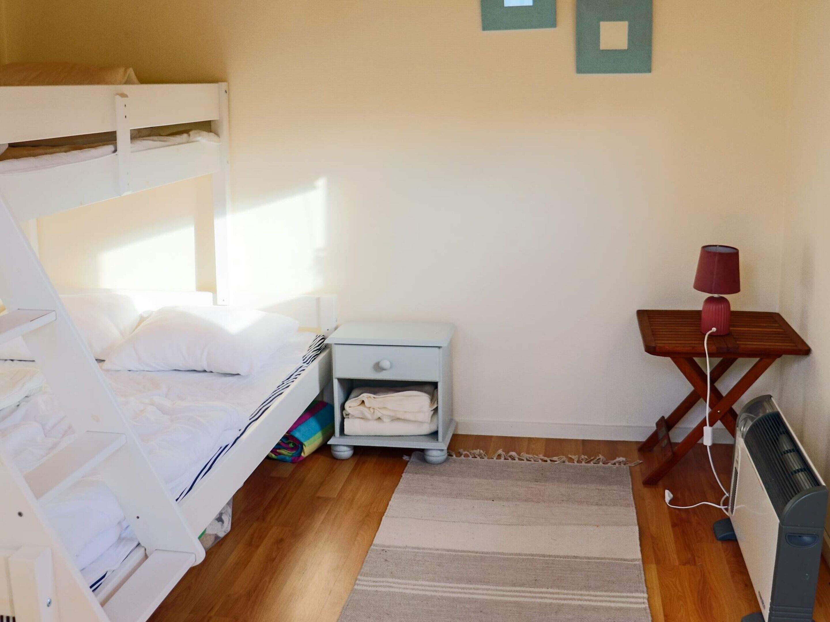 Une chambre avec un lit superposé, une petite table de chevet avec une lampe, un radiateur et un tapis.