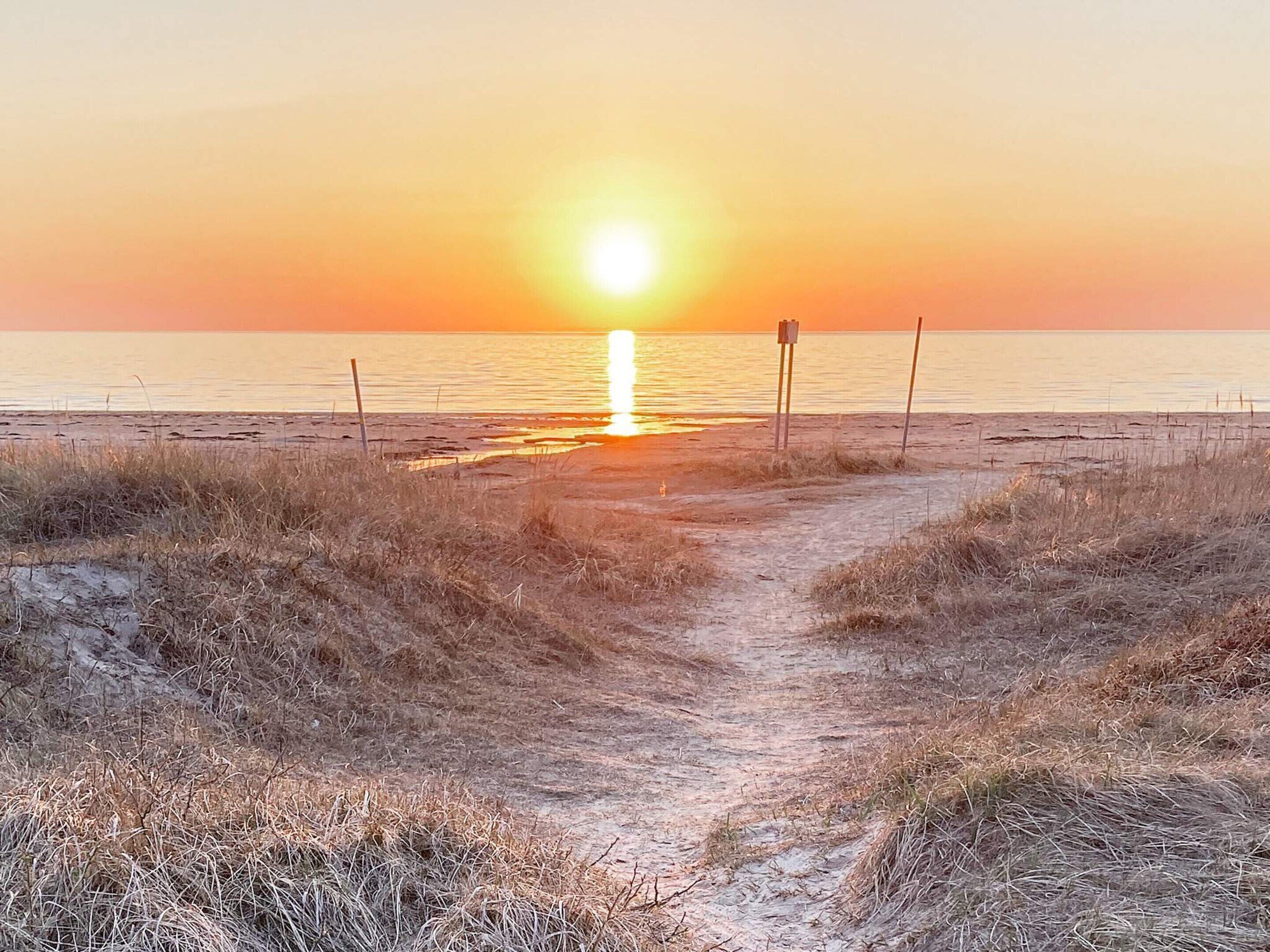 En strandpromenad som leder ner till havet, med en solnedgång i bakgrunden.
