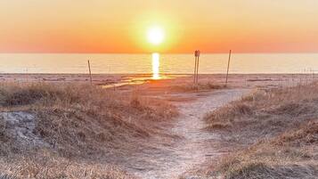 A beach path leading to the ocean with a sunset in the background.
