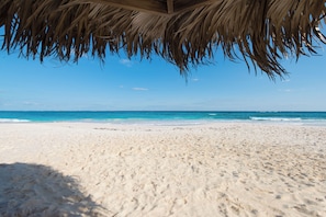 Una playa con una estructura de techo de paja, arena y un océano azul cristalino.