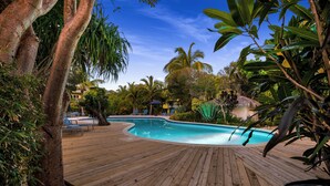 Ein Holzdeck umgibt einen Swimmingpool mit Liegestühlen und Palmen.