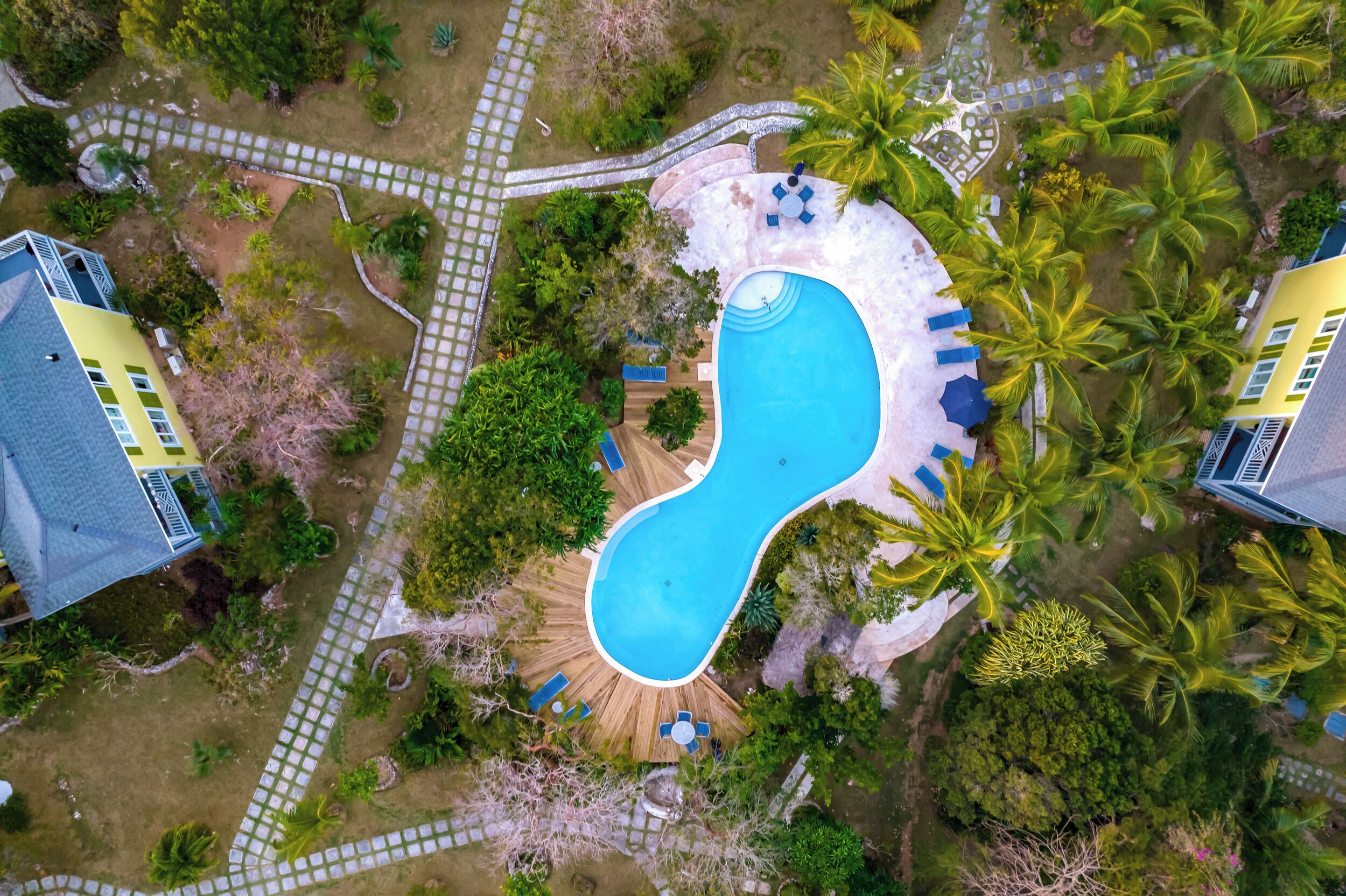 Ein Luftbild eines Resorts mit einem einzigartigen Infinity-Pool, umgeben von Palmen und einer Holzterrasse.