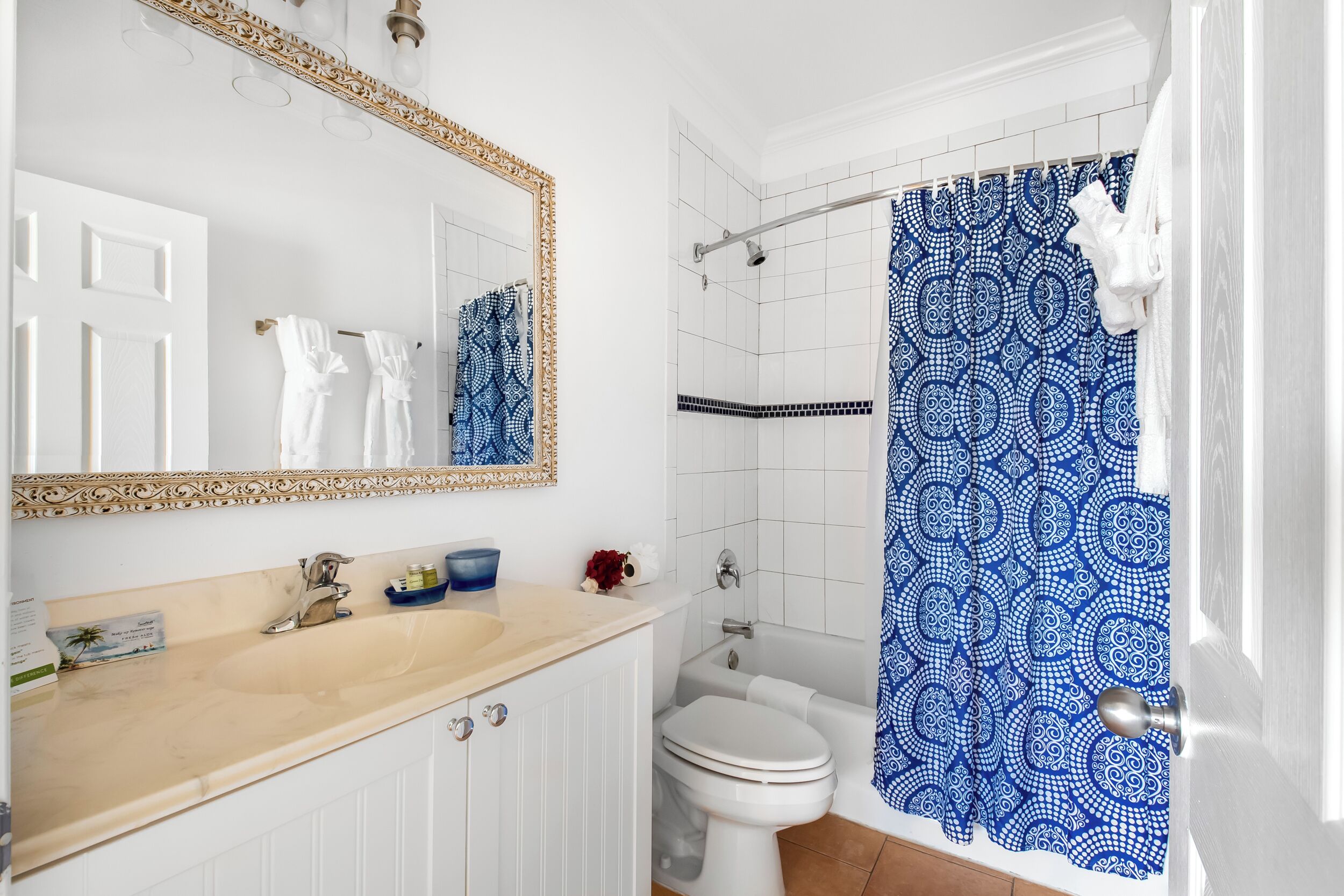 Ein Badezimmer mit einem beige farbenen Waschtisch, einer weißen Toilette und einem blauen, gemusterten Duschvorhang.