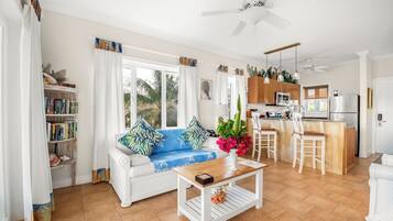 A bright living room with a sofa, coffee table, and a view of the kitchen.